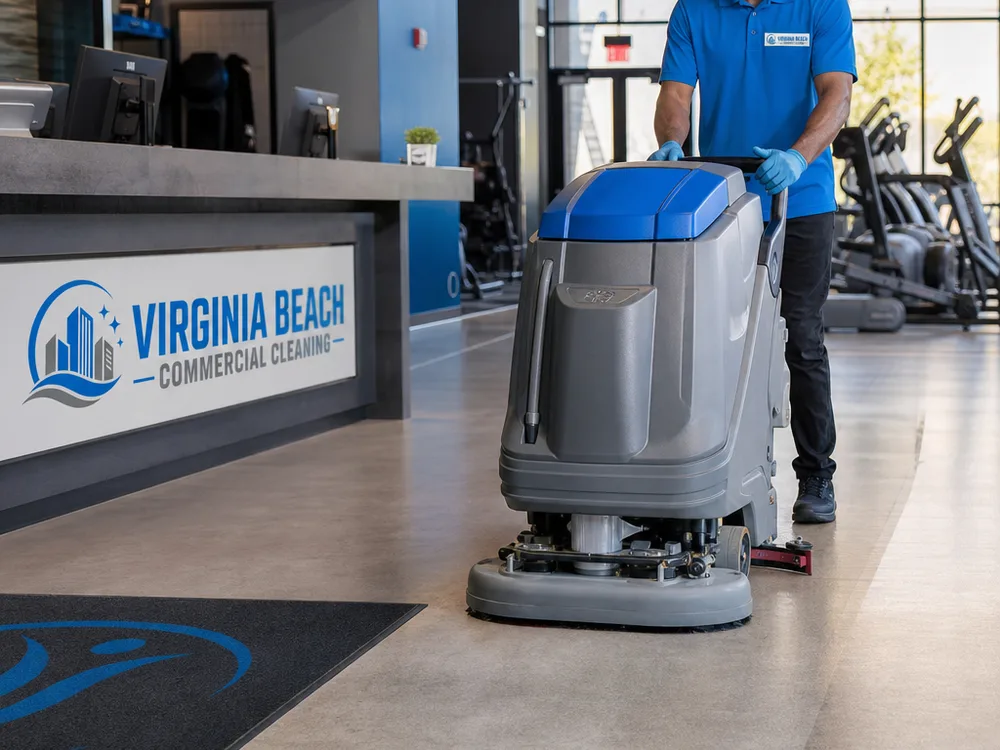 Auto-scrubber cleaning a wide gym walkway near the front desk with a clean path behind it